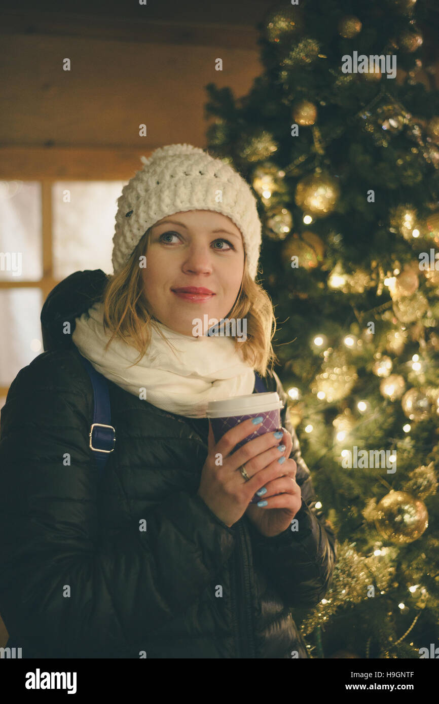 Glückliche junge Frau Kaffeetrinken am Weihnachtsmarkt in der Nähe von Weihnachtsbaum. Winter Urlaub Konzept Stockfoto