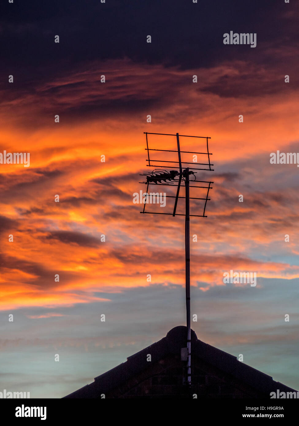 Silhouette-TV-Antenne und Hausdach gegen dramatischen Sonnenuntergang Stockfoto