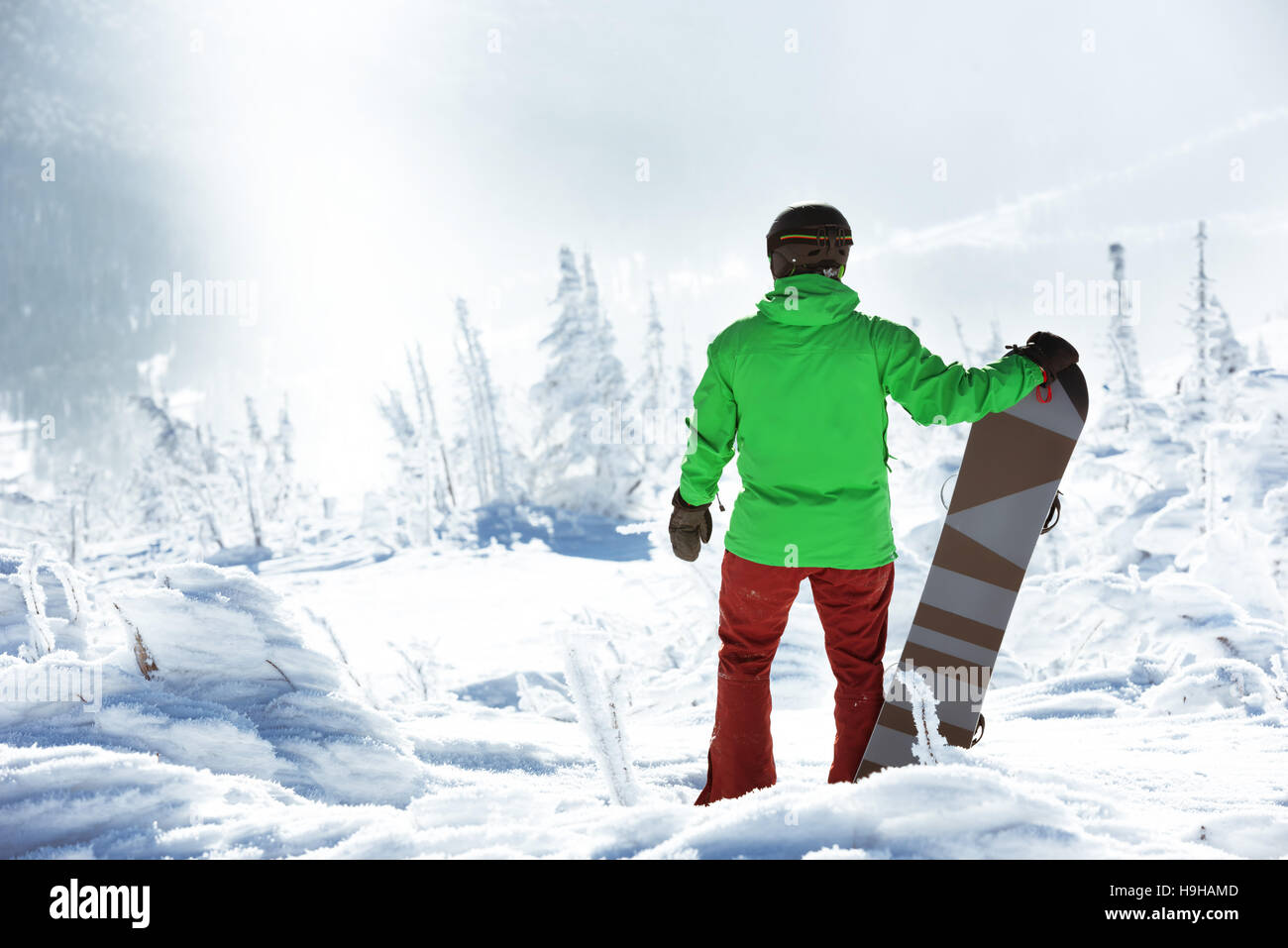 Snowboarder steht mit Snowboard auf Berggipfel auf Wald-Hintergrund. Sheregesh Skigebiet Stockfoto