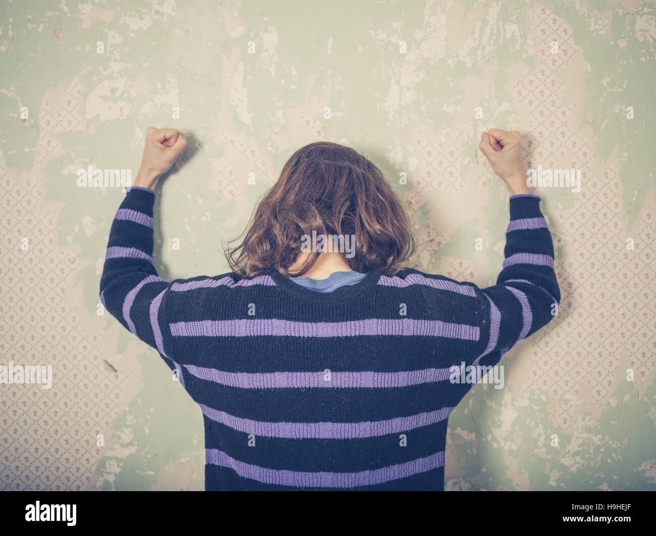 Eine frustrierte junge Frau ist ihre Fäuste gegen die Wand hämmern. Stockfoto