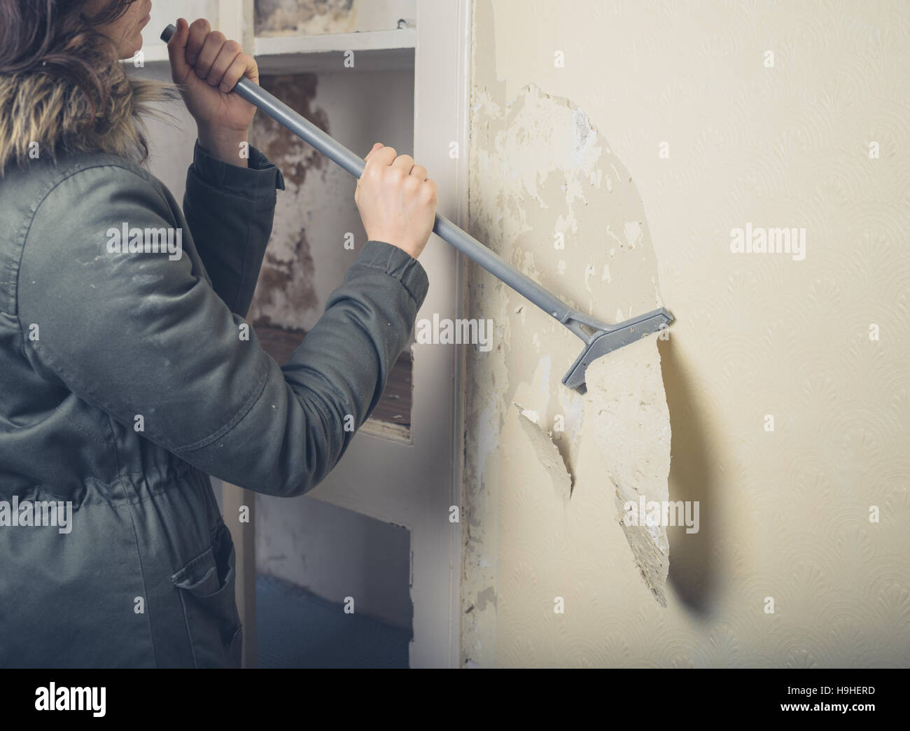 Eine junge Frau trägt einen warmen Wintermantel ist Renovierung eines Hauses und ist die Tapete abziehen Stockfoto