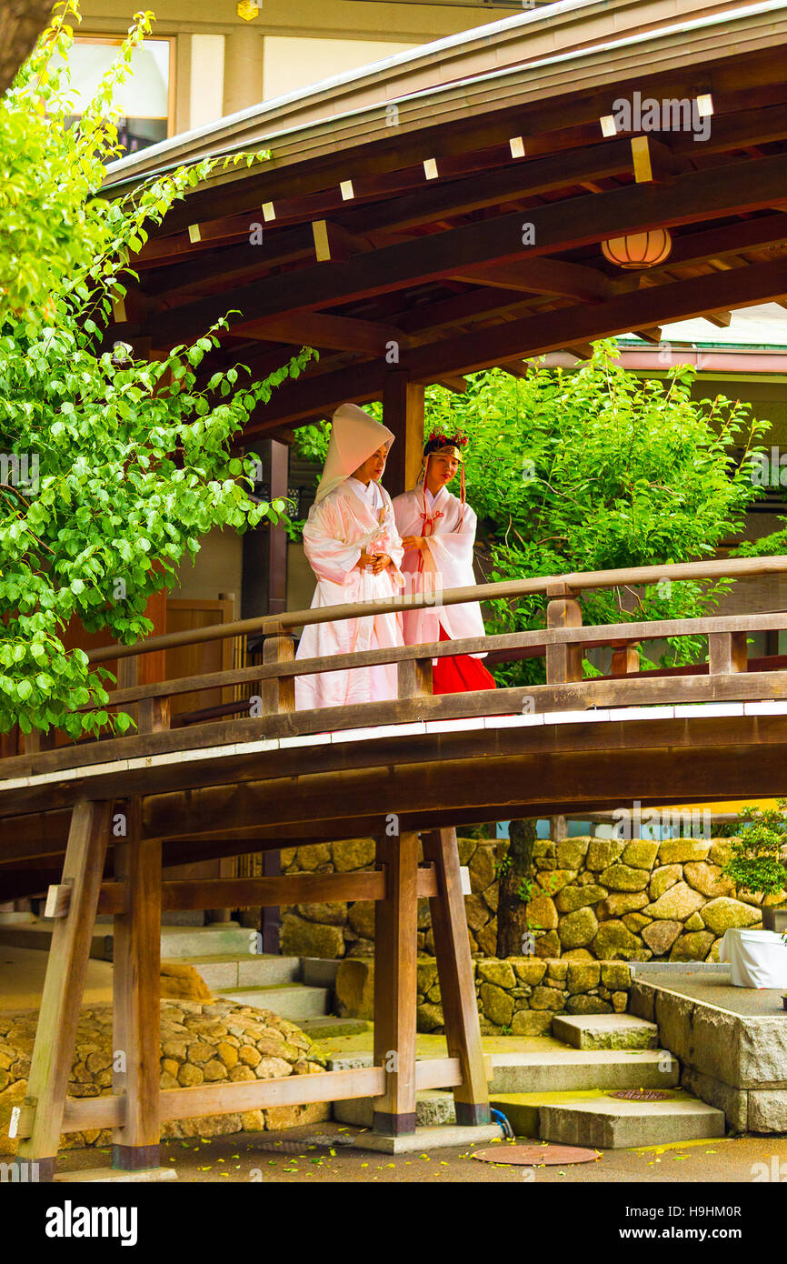 Eine Miko Jungfrau führt eine Braut im weißen traditionellen Kimono während einer Shinto Hochzeit hölzerne Brücke am Yushima Tenmangu Schrein Stockfoto