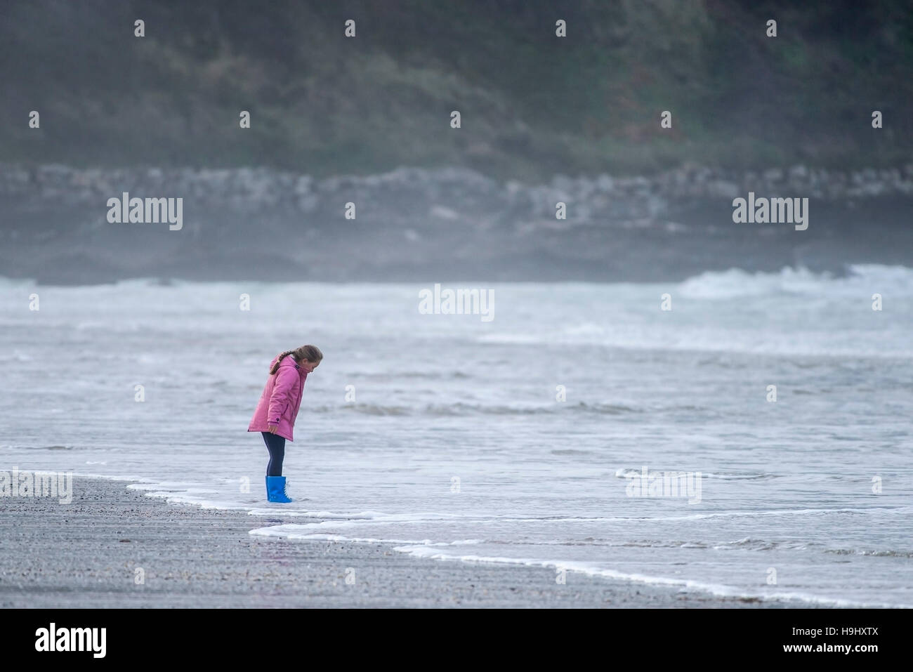 Ein junges Mädchen allein stehend an der Küste am Fistral Beach in Newquay, Cornwall. Stockfoto