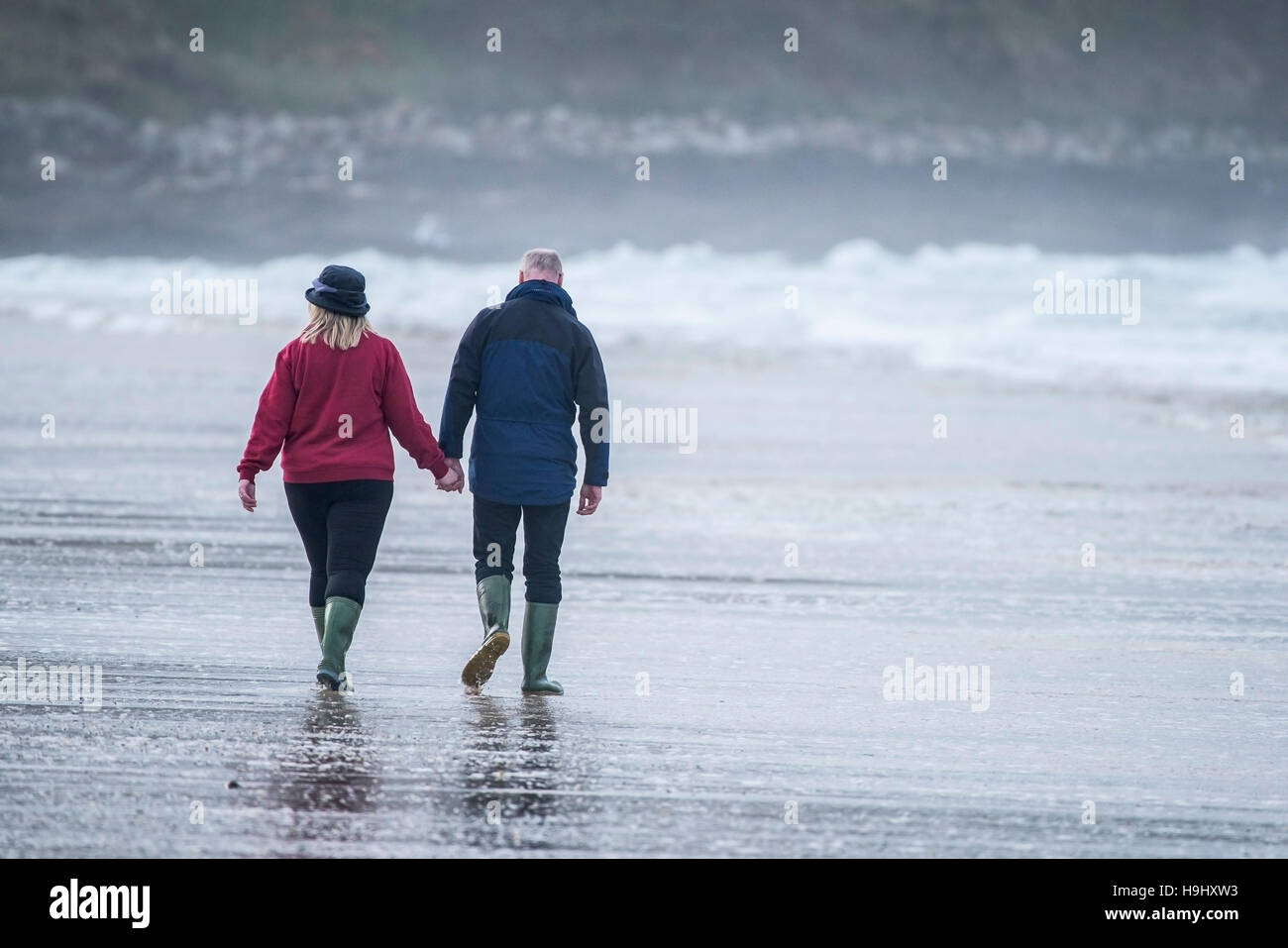 Ein paar halten Hände wie sie Fistral Beach in Newquay, Cornwall überqueren. Stockfoto