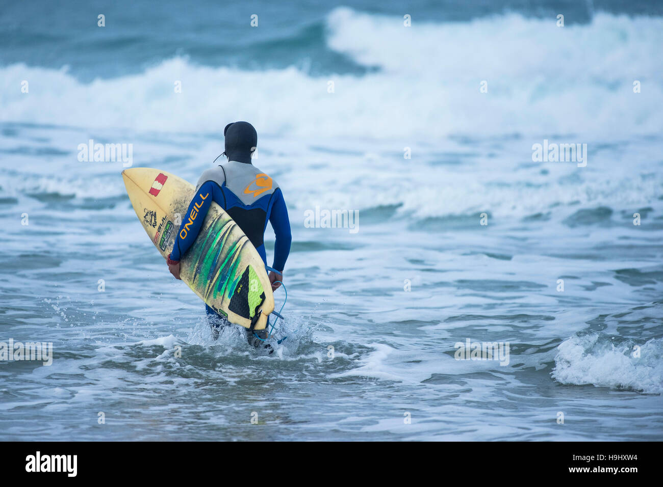 Ein Surfer mit seinem Surfbrett, als er am Fistral in Newquay, Cornwall ins Meer geht. Stockfoto