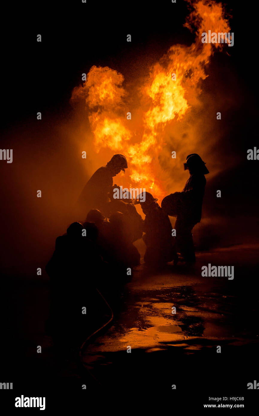 Silhouette der Feuerwehrleute kämpfen ein wütendes Feuer mit riesigen Flammen des brennenden Holzes Stockfoto