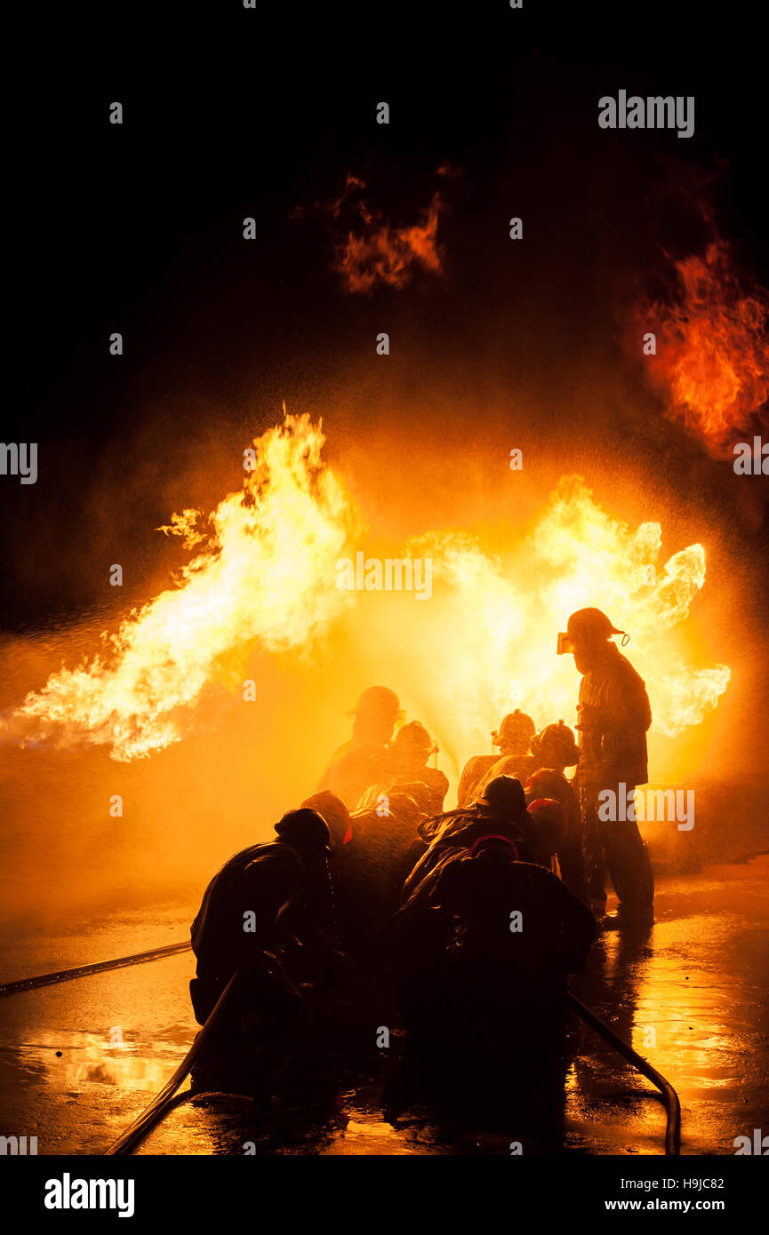 Silhouette der Feuerwehrleute kämpfen ein wütendes Feuer mit riesigen Flammen des brennenden Holzes Stockfoto