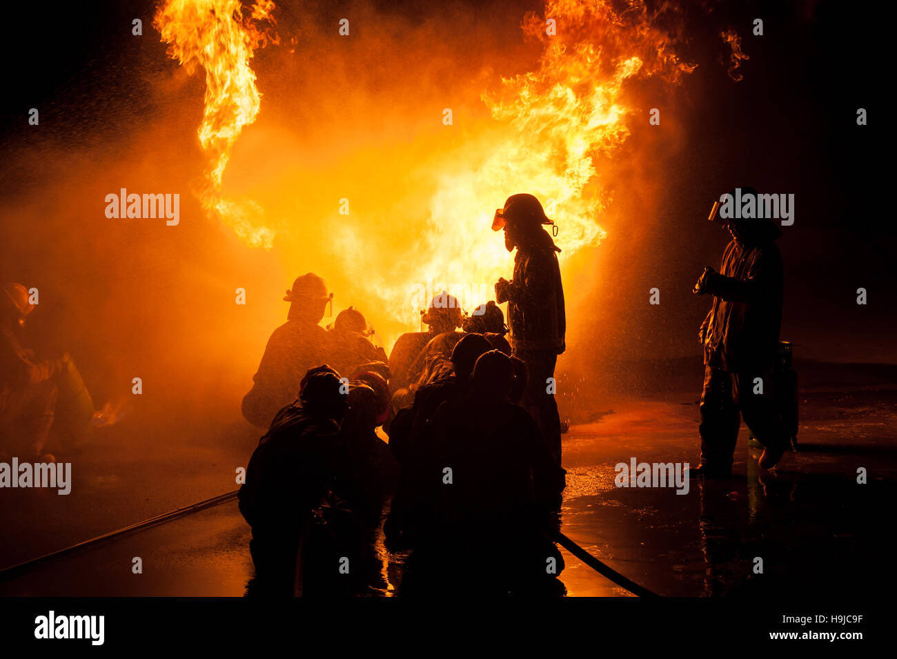 Silhouette der Feuerwehrleute kämpfen ein wütendes Feuer mit riesigen Flammen des brennenden Holzes Stockfoto