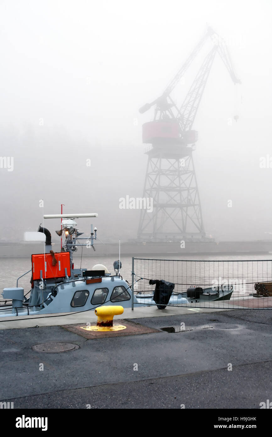 Kleines Handelsschiff in der Nähe von Birne auf Hintergrund mit großen Kran im Nebel Stockfoto