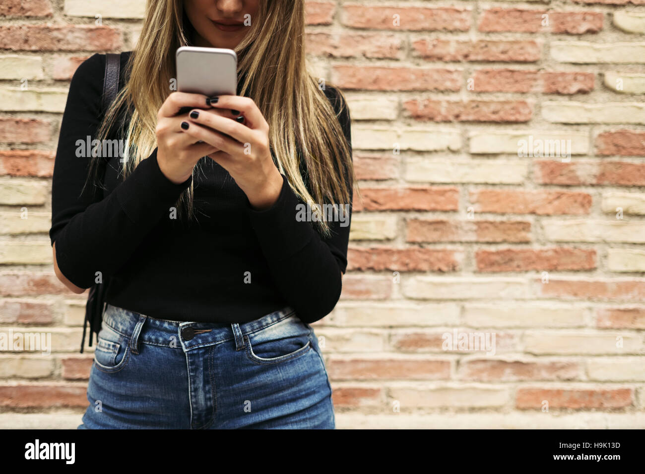 Junge Frau von SMS-Nachrichten vor Backsteinmauer Stockfoto