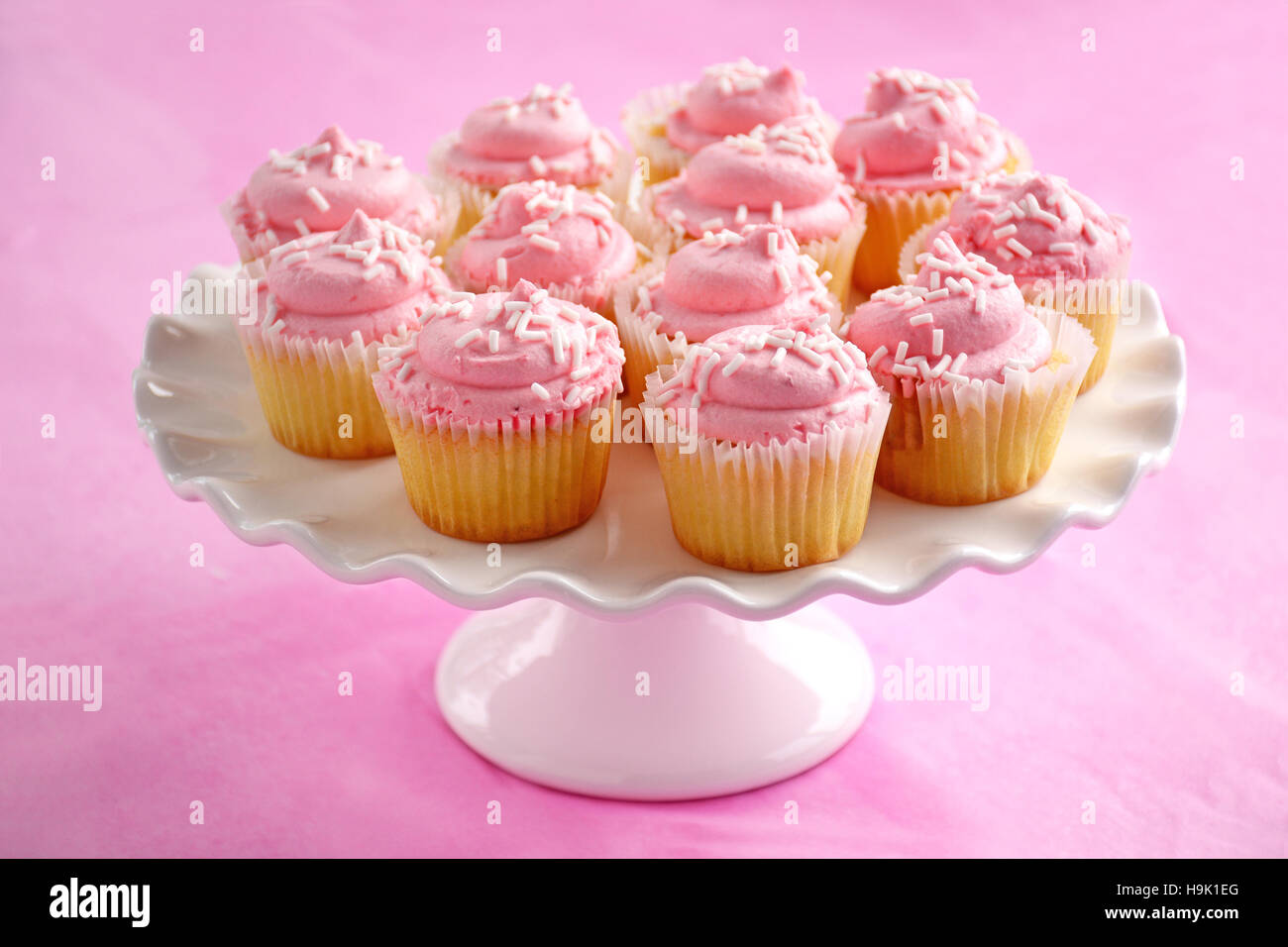 Zarte süße Mini Erdbeer Muffins auf weißen Sockel Kuchen stehen auf rosa Hintergrund im Querformat.  Geringe Schärfentiefe. Stockfoto