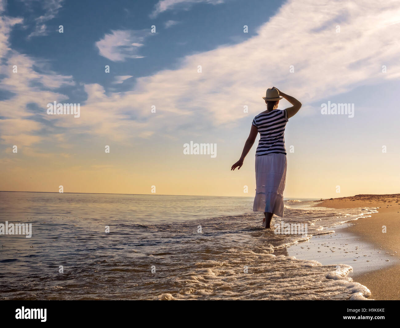 Junge Frau mit Hut und weißen Rock, ein Spaziergang entlang des Strandes in Richtung der aufgehenden Sonne Stockfoto