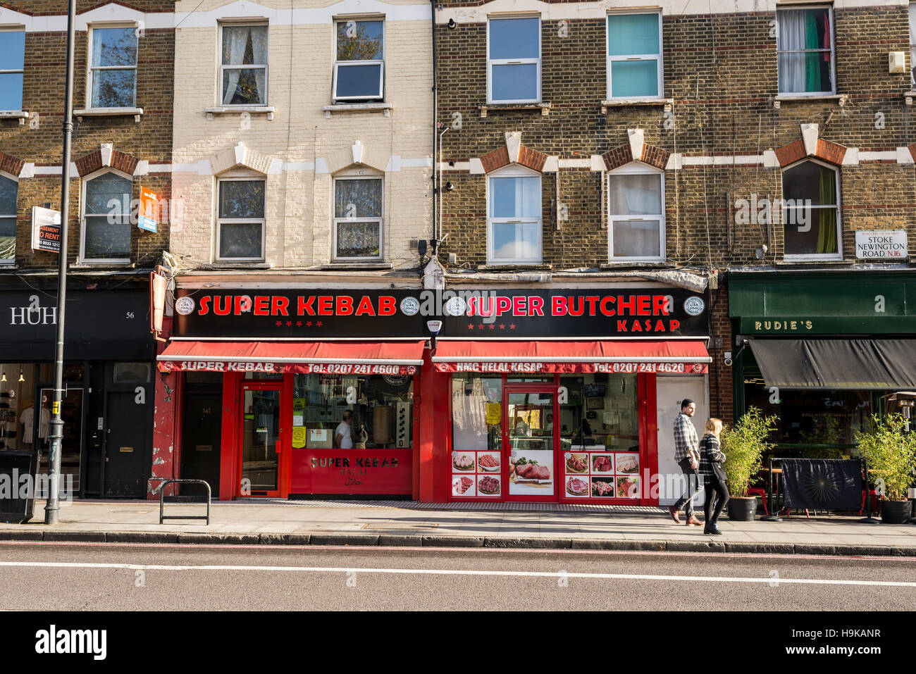 Passanten in Stoke Newington Road vor einem Kebab Restaurant und Metzgerei. In Dalston, East London gedreht. Stockfoto