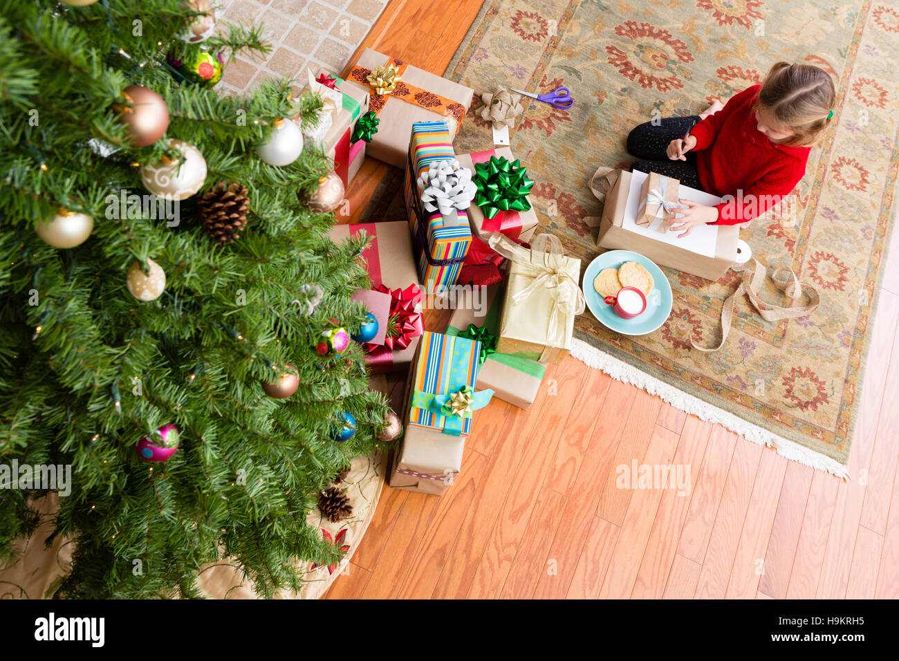 Kleine Mädchen ihren Brief an den Weihnachtsmann erzählt ihm von ihrer Träume für eine besondere Geschenke sitzt auf einem Teppich unten ein geschmückter Weihnachtsbaum in th Stockfoto