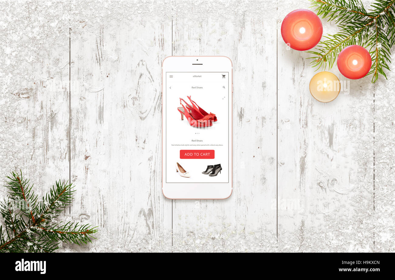 Shopping mit Smartphone in der Weihnachtszeit. Frau Schuhe in e-Commerce-Website oder App Draufsicht der weißen Holztisch. Stockfoto