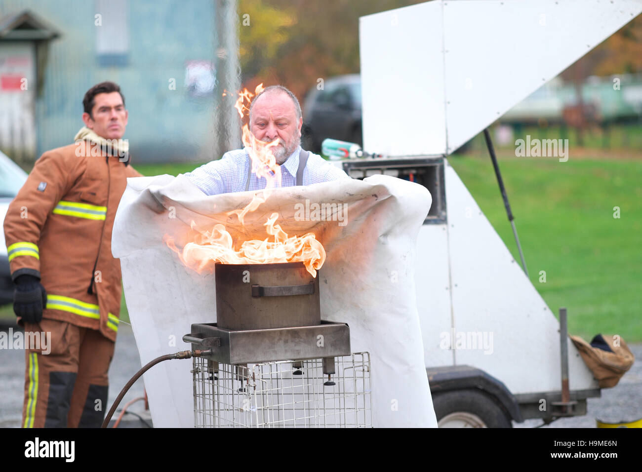 Gesundheit und Sicherheit auf der Baustelle Feuer Ausbildung mit einer Löschdecke um zu löschen Sie einen Topf mit Öl unter Anleitung UK Stockfoto