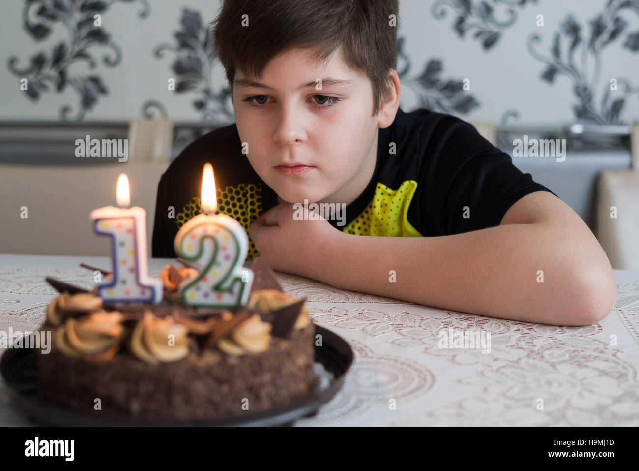 Teen Junge schaut nachdenklich Kuchen mit Kerzen am zwölften Tag der Geburt Stockfoto