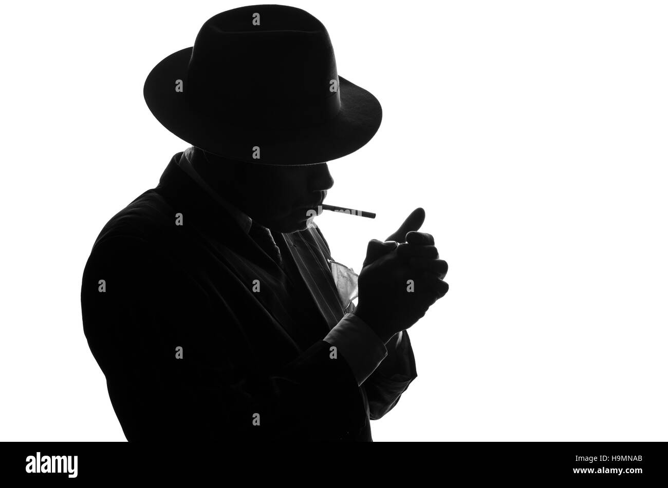 Silhouette der Privatdetektiv zündet die Zigarette. Agent sieht aus wie Al Capone bleiben Seite zur Kamera. Polizei kriminelle Szene in schwarz und weiß. Gangster-Studio gedreht Stockfoto