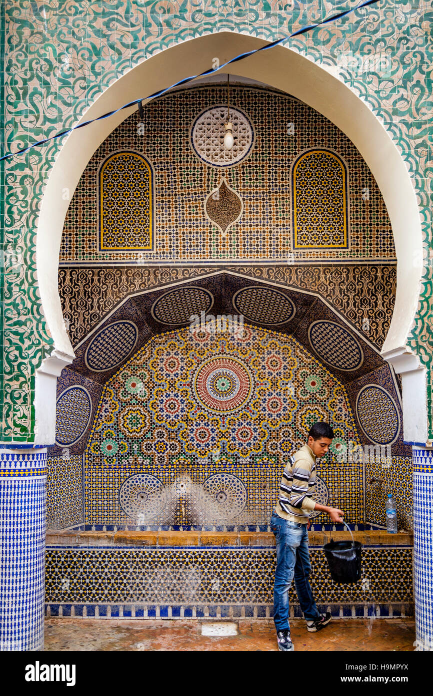 Eine junge Mann sammelt Wasser von A öffentliche Wasser Brunnen In der Medina, Fes el Bali, Fes, Marokko Stockfoto