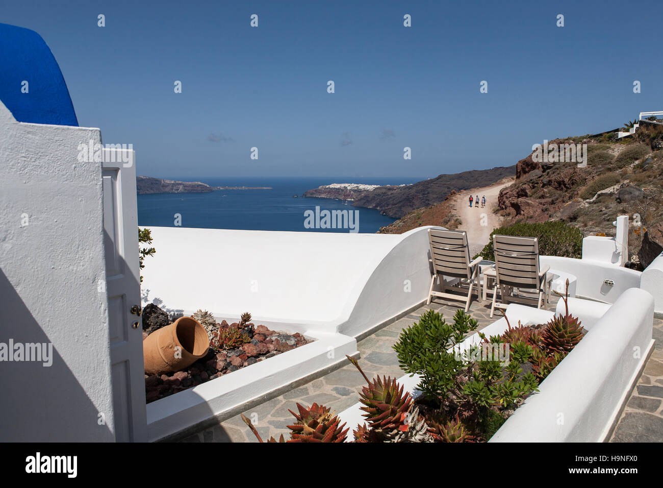 Terrasse mit 2 Stühlen mit Blick auf das Mittelmeer in Imerovigli, Santorin, Griechenland. Wanderer auf dem Weg nach Oia in der Ferne Stockfoto