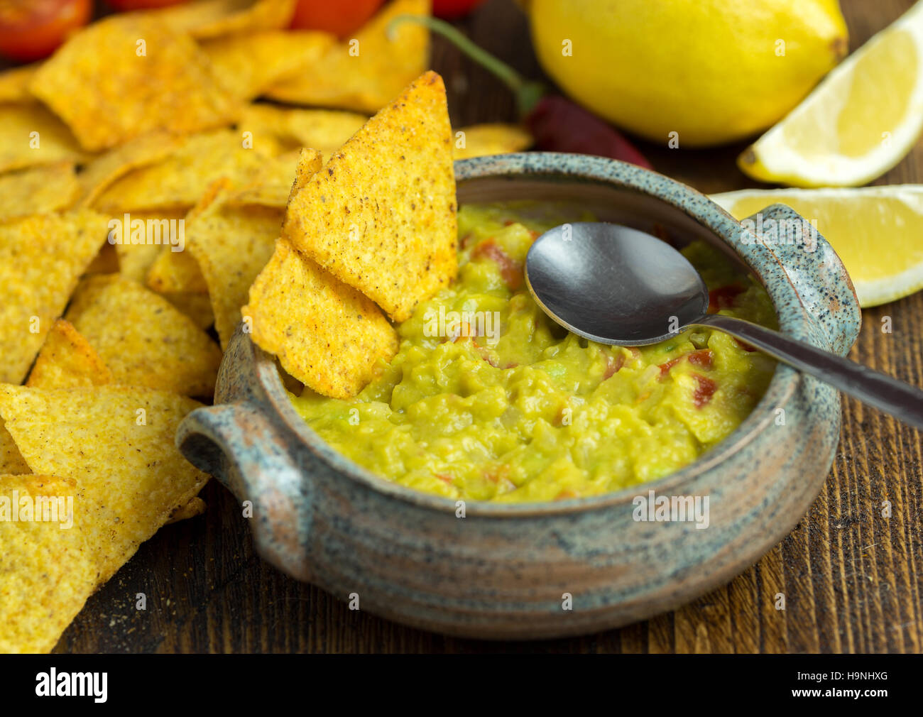 Guacamole in Hause gearbeitete Schüssel auf natürlichen hölzernen Schreibtisch mit Löffel im Inneren. Stockfoto