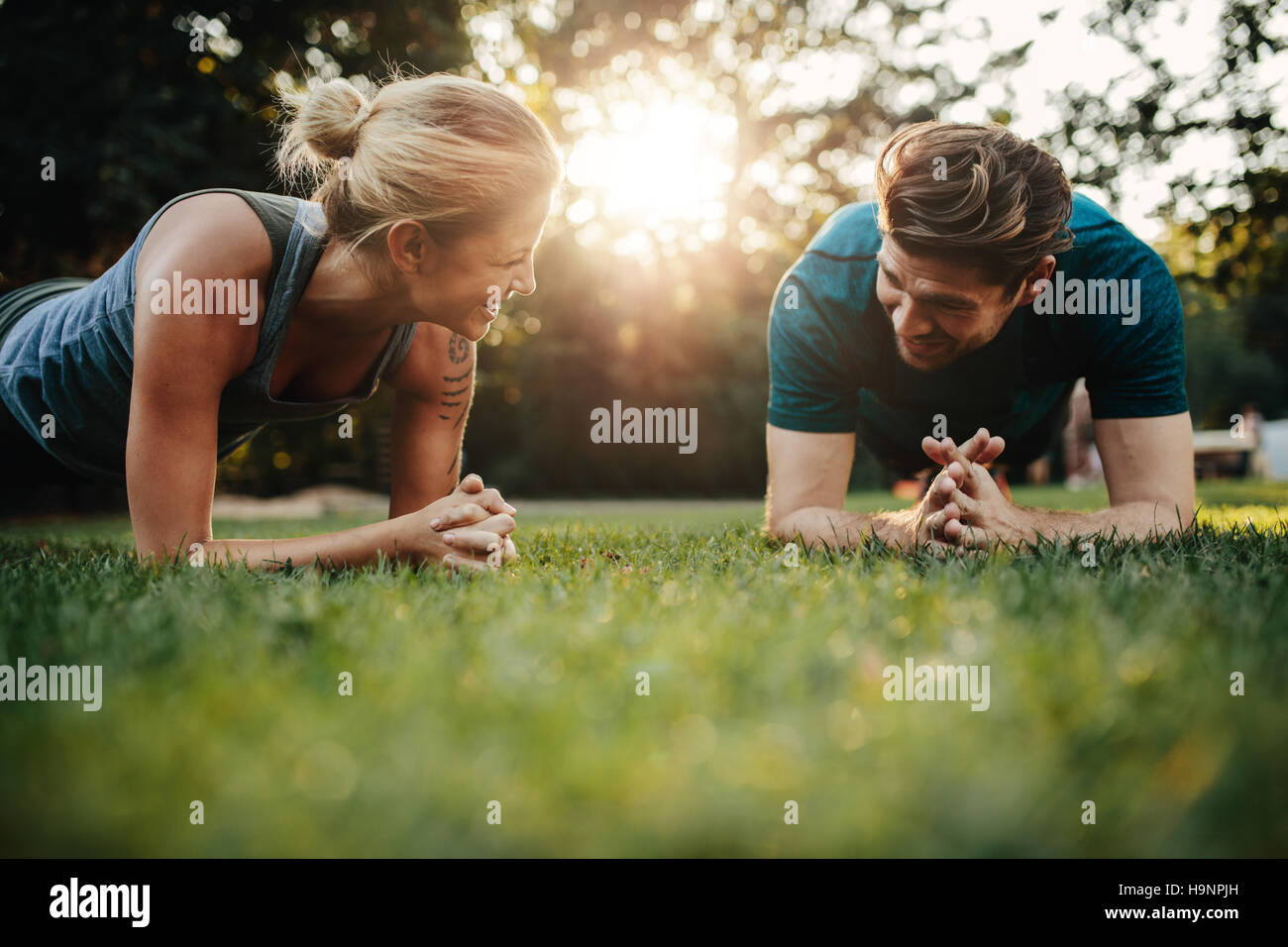 Passen Sie, junger Mann und Frau im Park trainieren. Lächelnde kaukasischen paar Core Training auf Rasen zu tun. Stockfoto