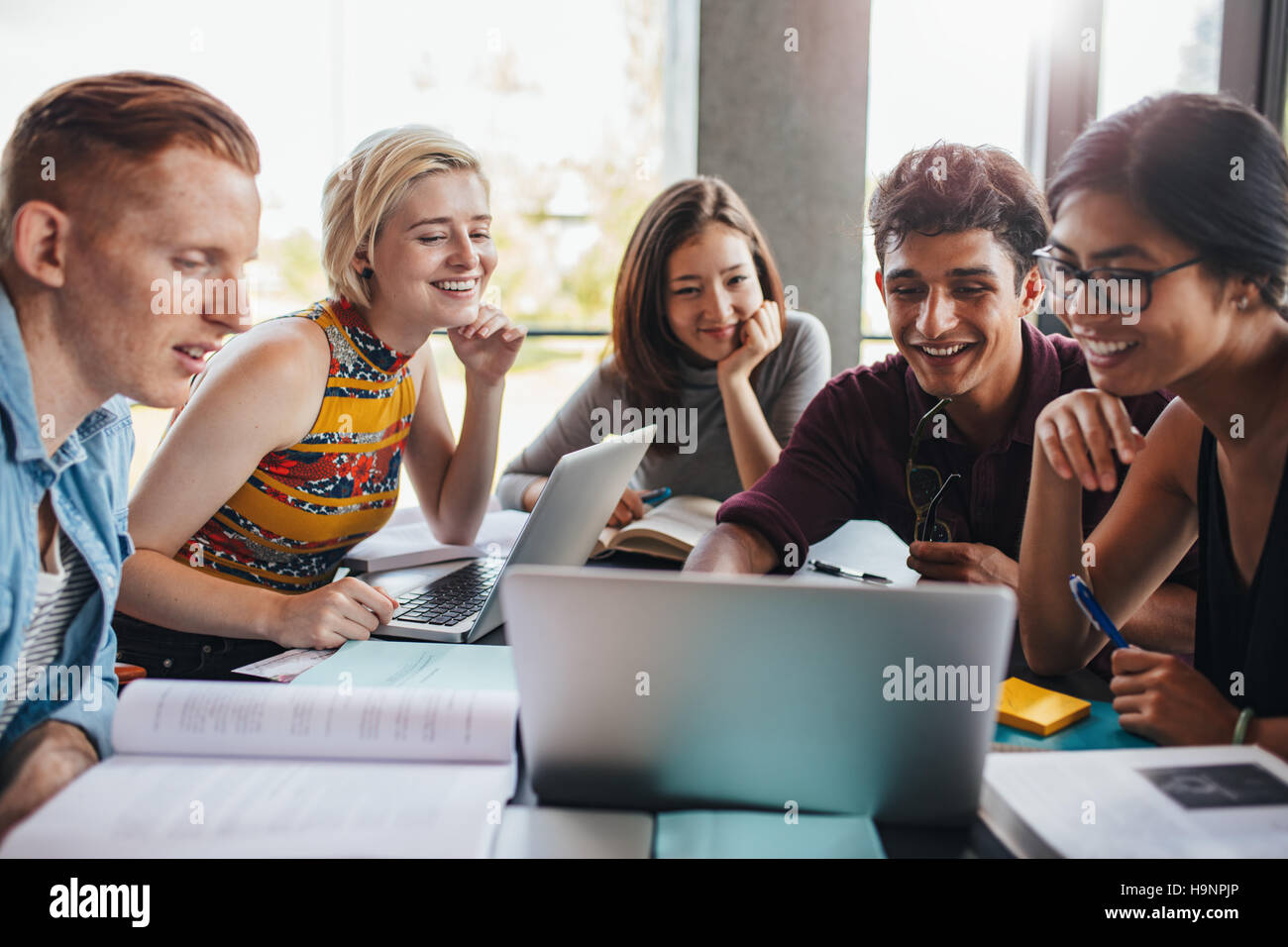 Gemischtrassigen Gruppe von jungen Studenten in der Bibliothek. Junge Menschen sitzen zusammen am Tisch mit Büchern und Laptop für die Erforschung der Informationen Stockfoto