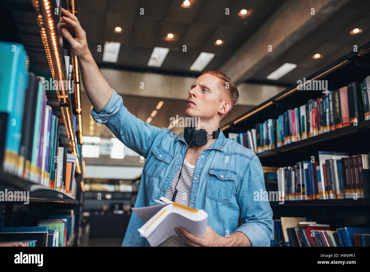Aufnahme des jungen männlichen Studenten, die Bibliothek Regal Buch auswählen. Studentin in der Bibliothek zu studieren. Stockfoto