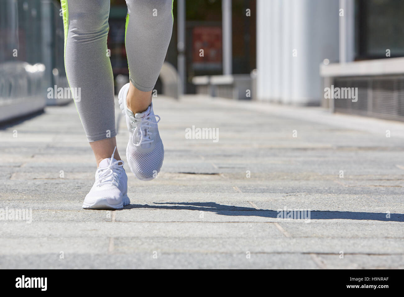 Frau läuft in der Stadt mit Trainingsanzug und weiße Schuhe, Sonnenlicht Stockfoto