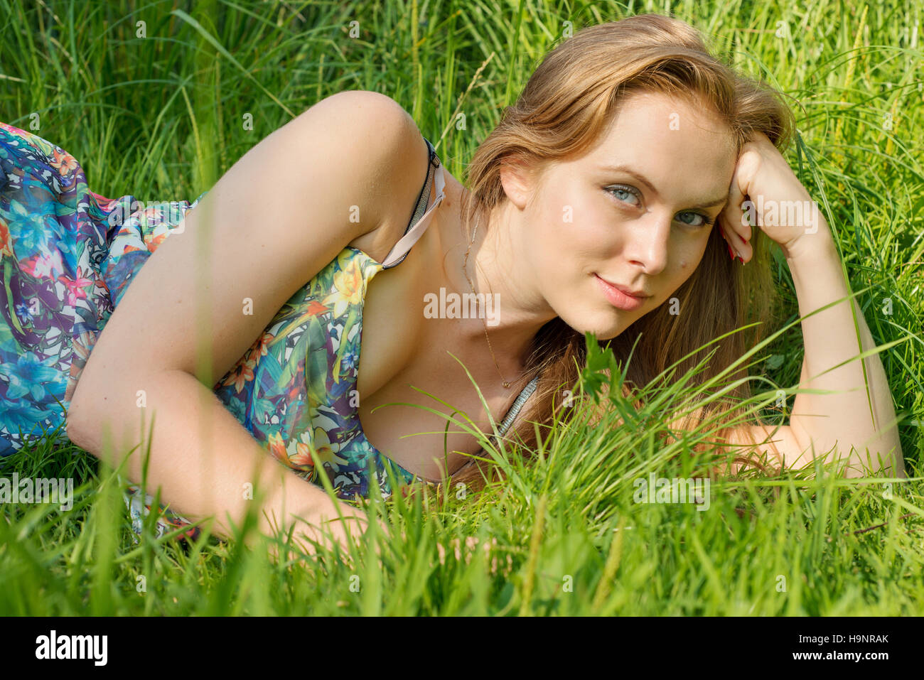 Junge Frau mit langen Haaren, die im Sommer auf der Wiese liegend Stockfoto