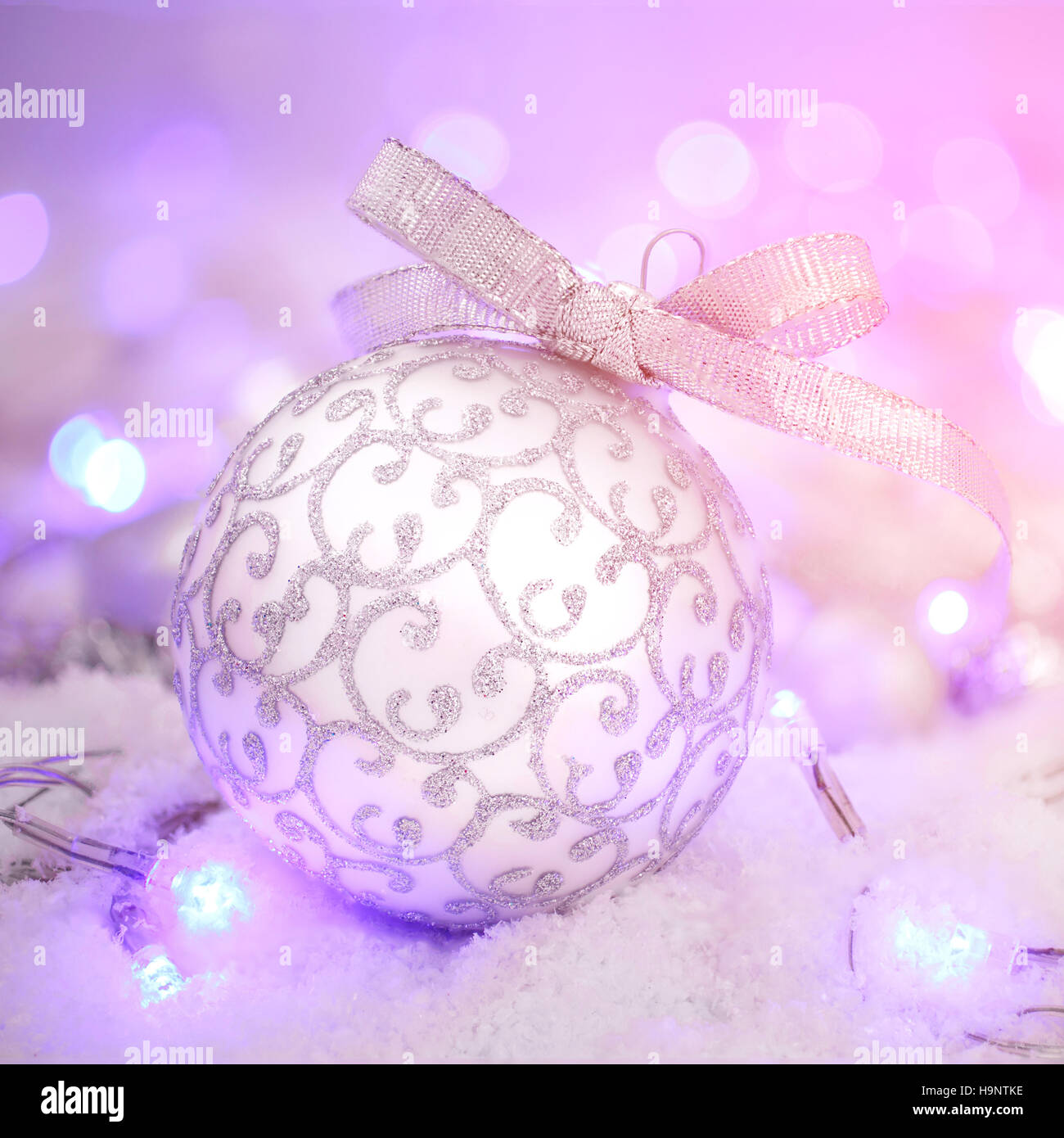 Silberne Weihnachtskugel und Schnee auf lila Bokeh Stockfoto