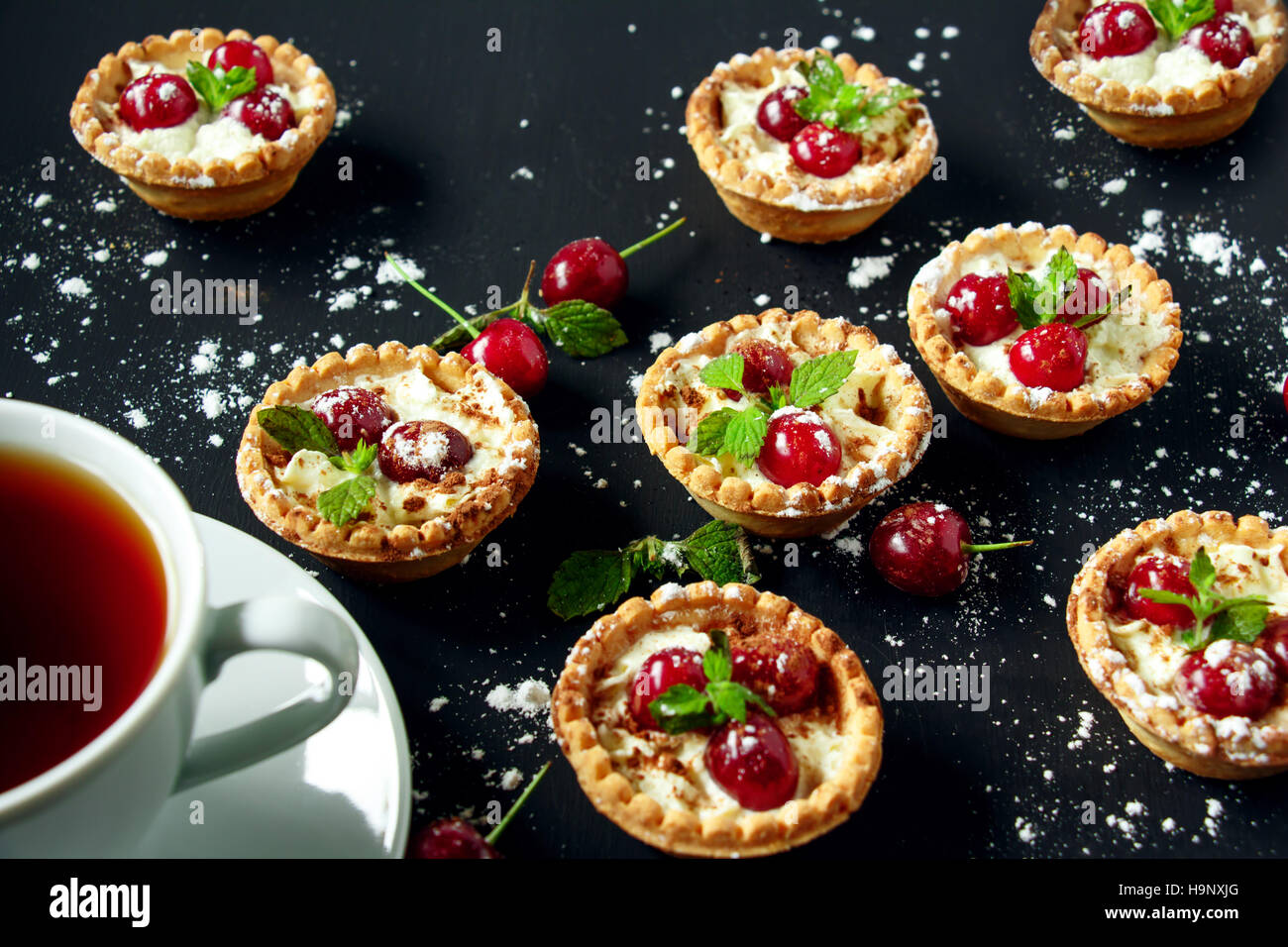 Törtchen mit Sahne und Kirsche auf einem schwarzen Hintergrund. Selektiven Fokus. Stockfoto