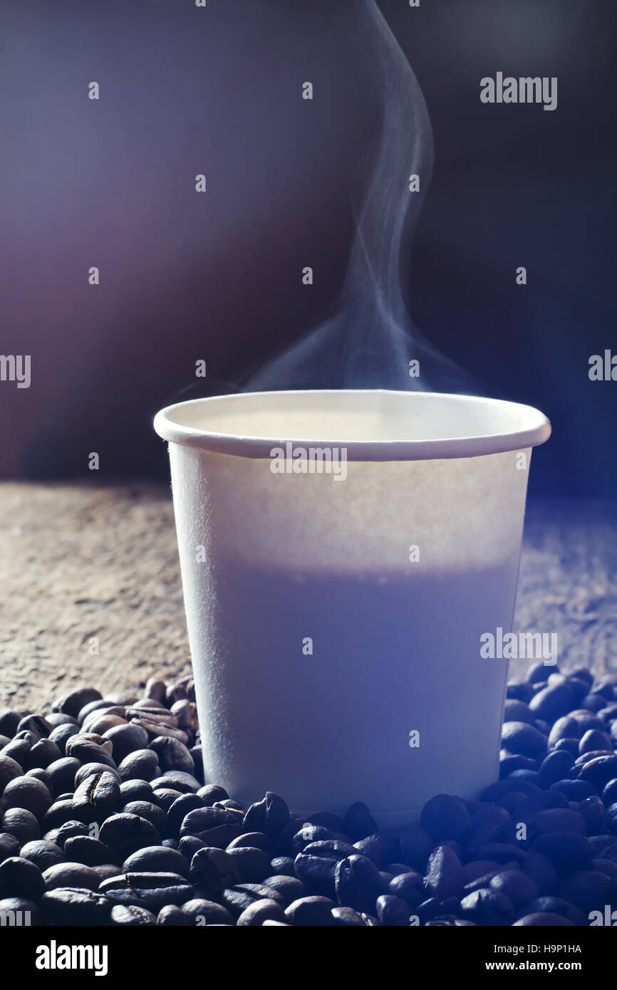 Pappbecher frischen heißen Kaffee mit Rauch und Kaffee Bohnen auf Holztisch. Stockfoto