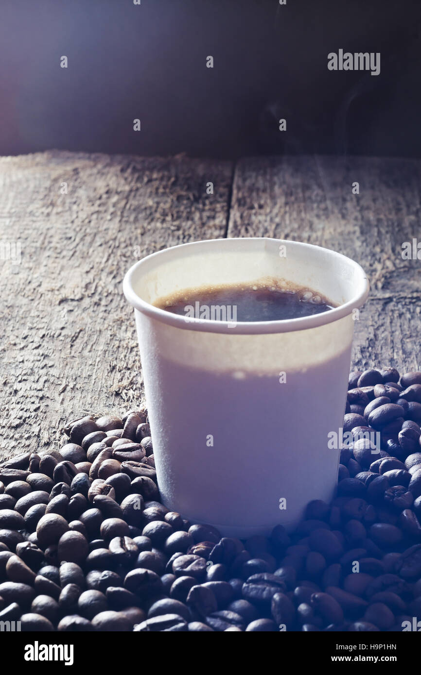 Pappbecher frischen heißen Kaffee mit Rauch und Kaffee Bohnen auf Holztisch. Stockfoto