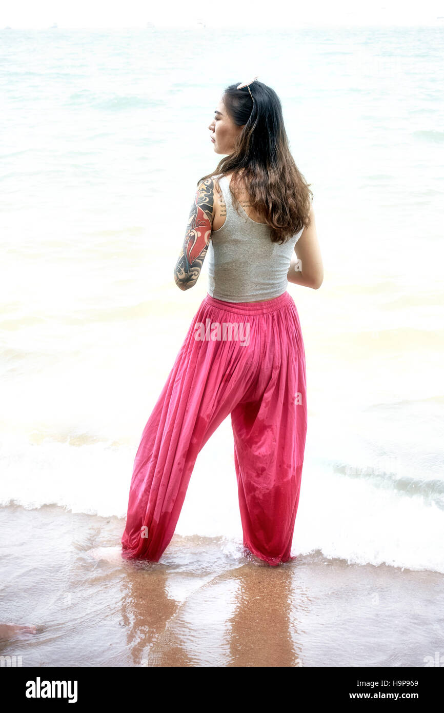 Frau trägt rote Pantaloon-Hose und zu Fuß im Meer am Pattaya Strand Thailand S. E. Asien Stockfoto