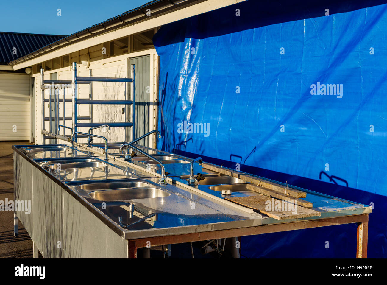 Alte Küchenspüle außerhalb einer öffentlichen Toilette, die renoviert wird. Blaue Plane Abdeckung Teil des Gebäudes. Stockfoto