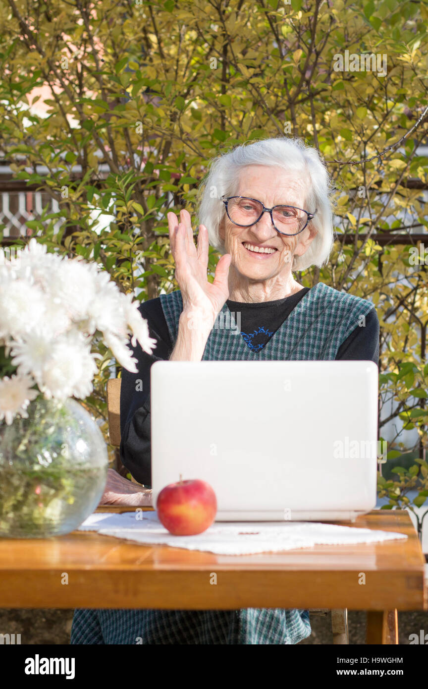 90 Jahre alte Frau winkt mit einem einen Videoanruf auf einem weißen Notebook Stockfoto