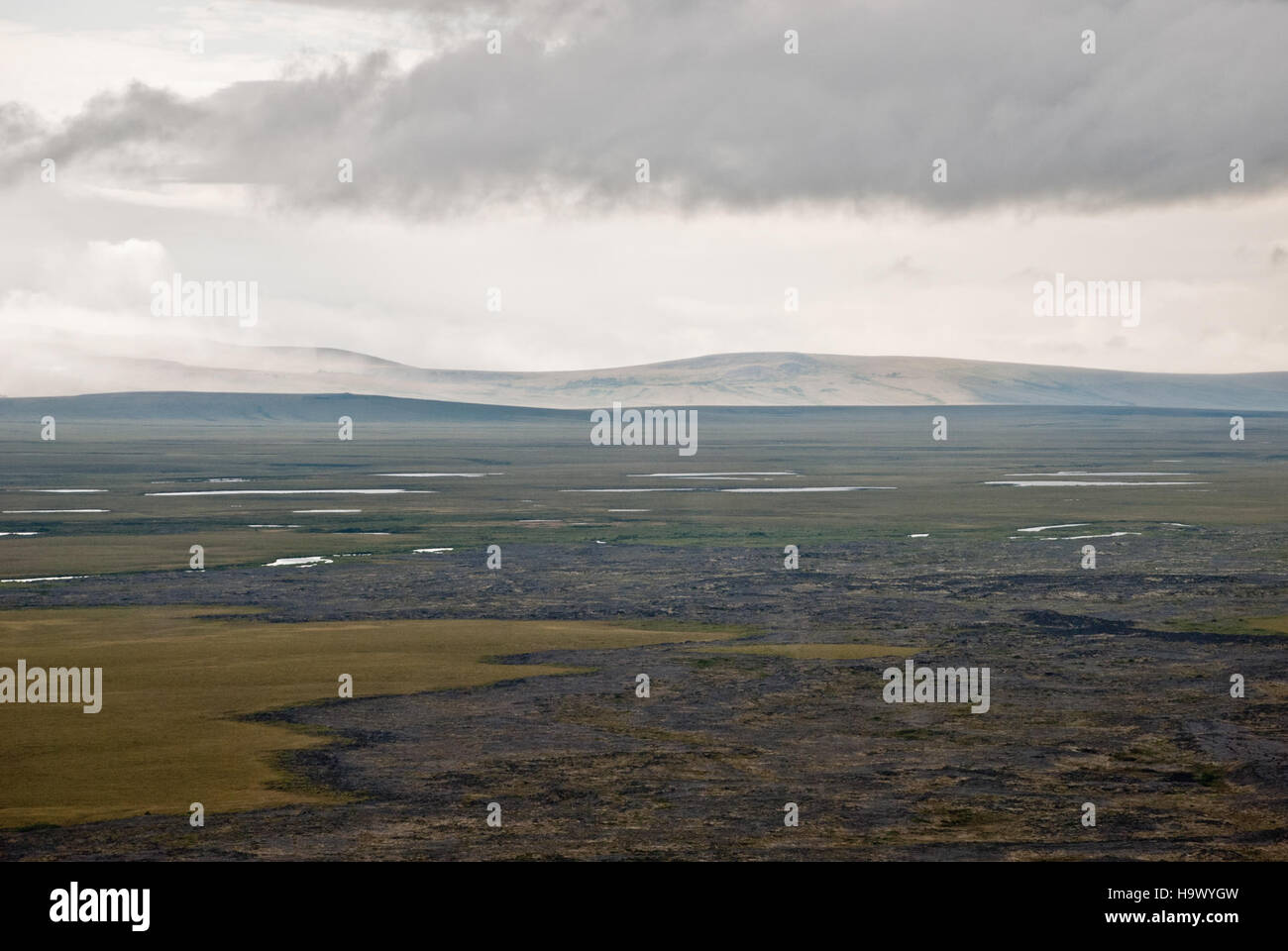 Dieses Bild zeigt einen dramatischen Blick auf die Bering Land Bridge, mit einem fließenden Lavafeld und fernen Regenfällen, die an eine dynamische natürliche Landschaft in der Region der Beringstraße erinnern. Stockfoto