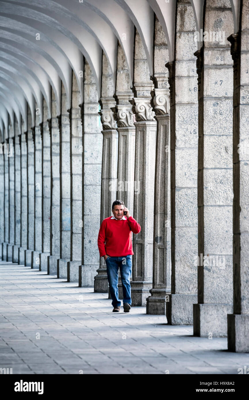 Mann im roten Pullover, spricht auf Handy, zu Fuß durch Säulen und Bögen, Plaza de Armas, Arequipa, Peru Stockfoto