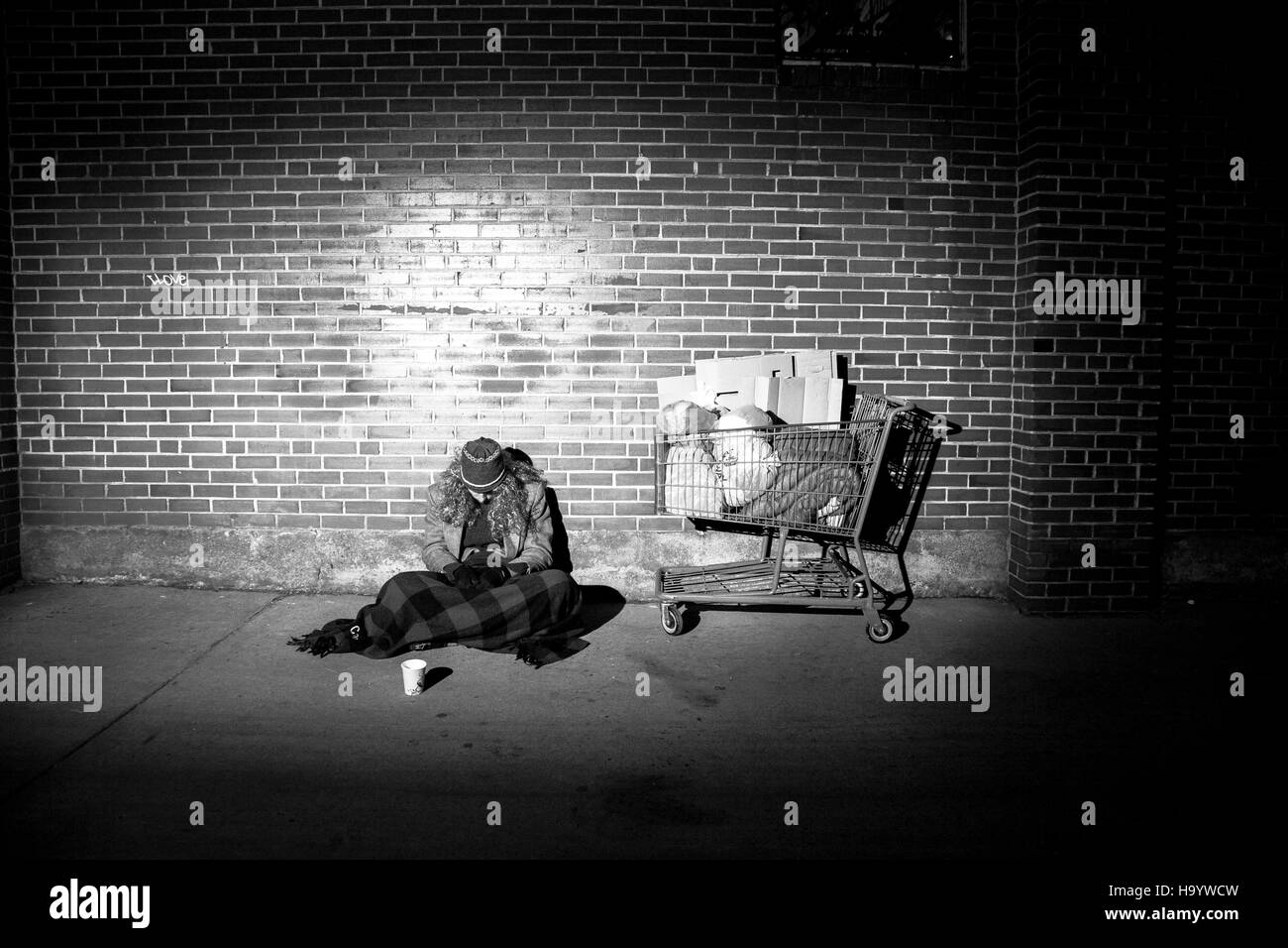 Modellierte, inszenierten Schuss ein Obdachloser Mann betteln auf dem Bürgersteig mit gesenktem Kopf, nicht in die Kamera schaut. Stockfoto