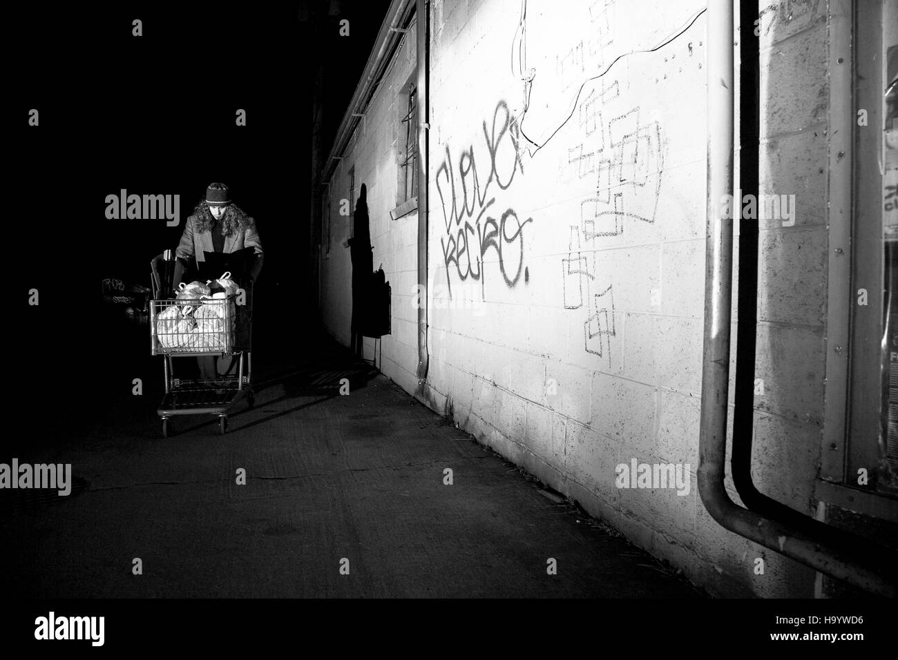 Modellierte, inszenierten Schuss Darstellung einen Obdachlosen Mann schob einen shopping cart durch eine Gasse. Stockfoto
