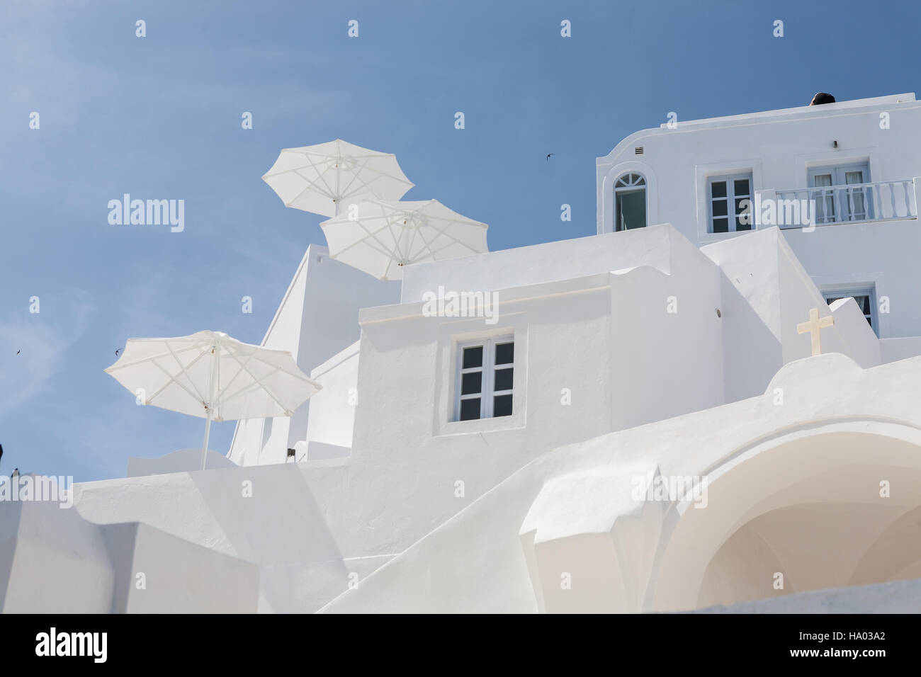 Weiß getünchte Hotel-Fassade mit weißen Patioregenschirme an einem sonnigen Tag in Imerovigli, Santorin, Griechenland Stockfoto