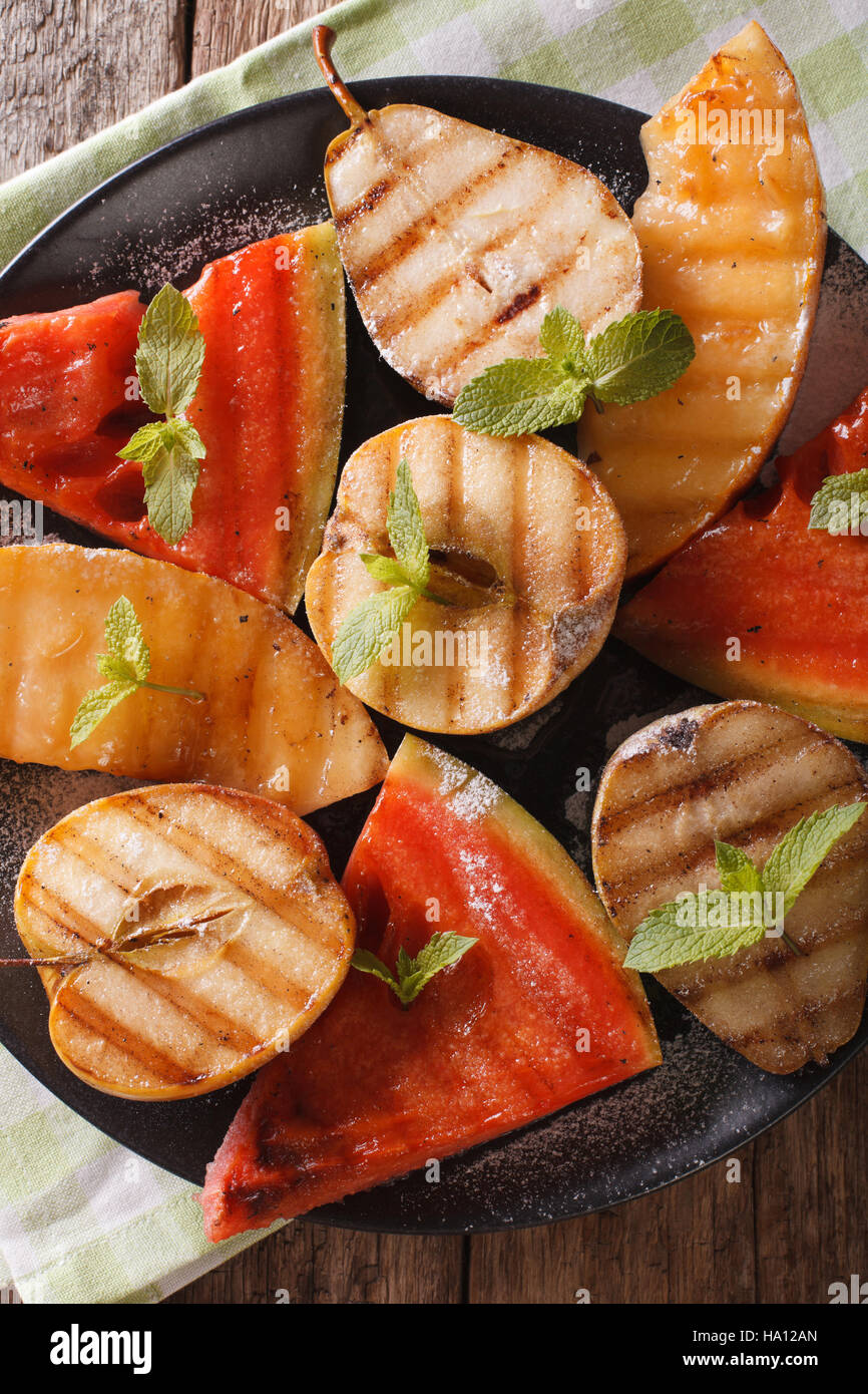 Gegrilltes Obst: Wassermelone, Melone, Apfel, Birne auf einer Platte Makro. vertikale Ansicht von oben Stockfoto