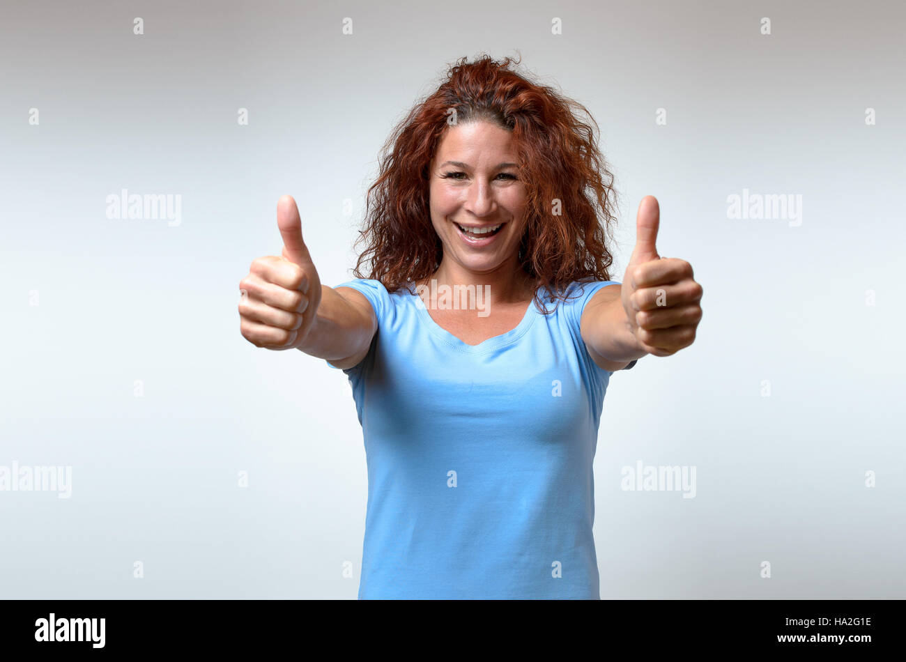 Begeisterte motivierte attraktive junge Frau geben einen Daumen nach oben Geste der Zustimmung und der Erfolg mit einem strahlenden Lächeln Stockfoto