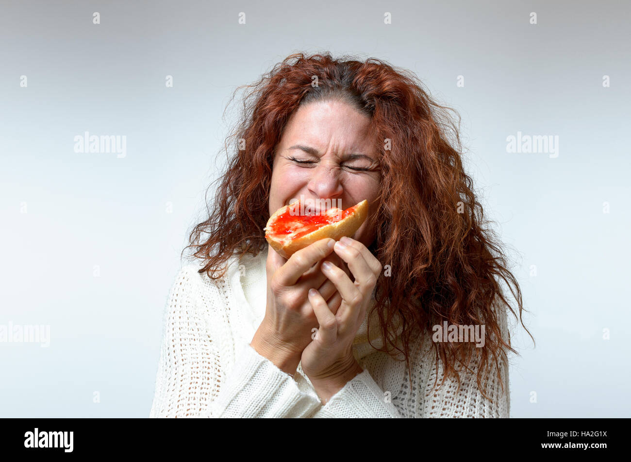 Junge Frau mit langen Locken tragen stilvolle Herbstmode beißen in einen  bunten roten Beeren Marmelade Sandwich auf einem knusprigen Brötchen mit  einem Blick lustvoll, h Stockfotografie - Alamy