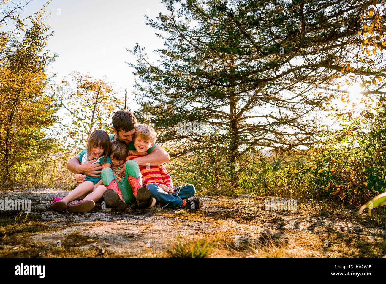Vater sitzt im Wald drei Kinder umarmen Stockfoto