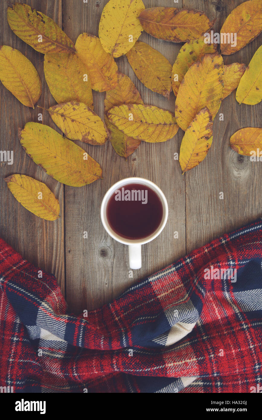 Flache Laien Blick auf Herbstlaub und strukturierte Tartan Schal auf hölzernen Hintergrund mit Tasse Tee - Herbst-Konzept Stockfoto