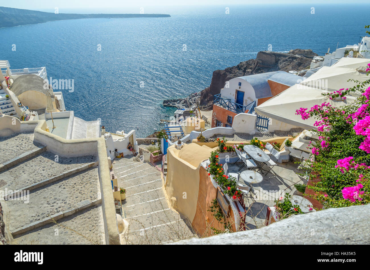 Traditionelles Santorini felsigen Architektur, mit wunderschönen Blick auf Caldera, Stufen hinunter zum Meer und kleine Taverne mit Blumen Stockfoto