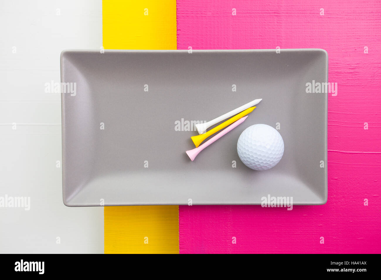 Graue Keramik Teller mit Golf-Ausrüstungen auf über weiß, gelb und rosa Holztisch, Rechteck Schale Stockfoto