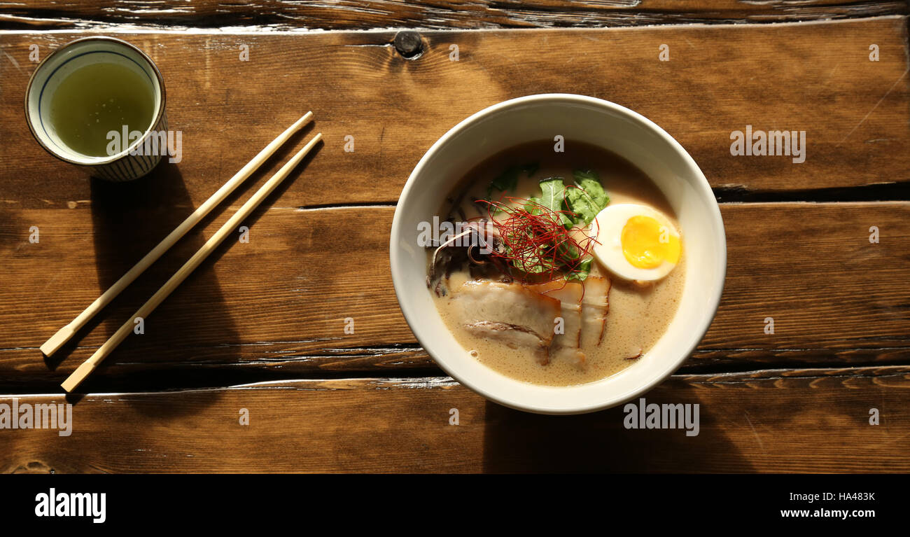 Mittags Schüssel mit japanischen Nudeln und Ramen-Brühe mit Essstäbchen und Teetasse auf rustikalem Holztisch Stockfoto